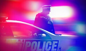 Police officer standing beside a patrol car with emergency lights flashing.