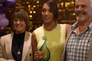 Mila Reuelu-Buchanan holding a green glass award, standing between two supporters at the Stars Awards Night in Karaka. Ask ChatGPT