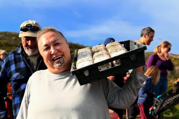 Hikitia Ropata smiling and carrying a tray of seedlings at the Whitireia Park restoration planting event.