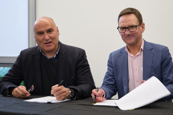 Helmut Modlik and Nigel Corry seated at a table signing documents during the lease agreement ceremony between Ngāti Toa Rangatira and Greater Wellington.