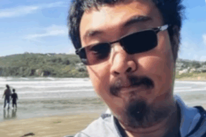 Jinting Guo wearing sunglasses and looking at the camera with a beach and ocean in the background