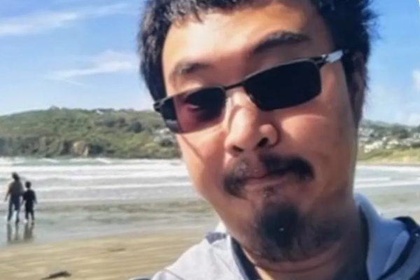 Jinting Guo wearing sunglasses and looking at the camera with a beach and ocean in the background