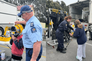 Two children interacting with New Zealand Police Dive Squad officers and trying on diving equipment during a holiday event.