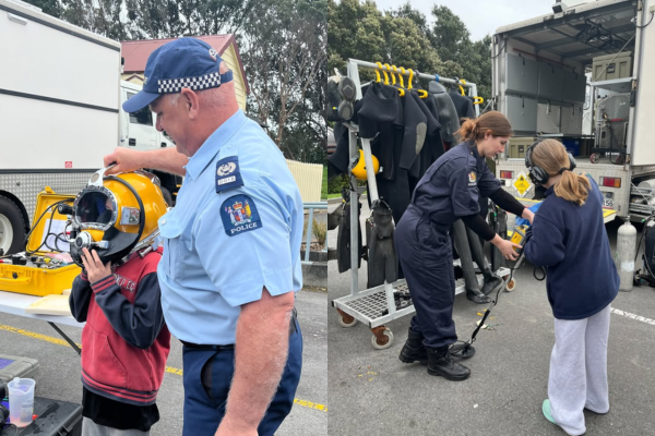Two children interacting with New Zealand Police Dive Squad officers and trying on diving equipment during a holiday event.