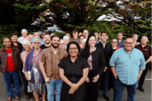 Barbara Edmonds standing in front of a large group of smiling supporters outdoors.