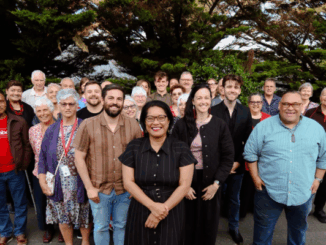 Barbara Edmonds standing in front of a large group of smiling supporters outdoors.