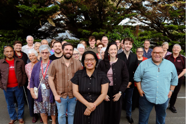 Barbara Edmonds standing in front of a large group of smiling supporters outdoors.