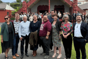 Group photo of Porirua City councillors and Mayor Anita Baker standing in front of a carved wharenui at the Council’s 2025–28 swearing-in ceremony
