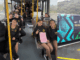 Group of school-aged children sitting inside a community bus and smiling at the camera; side view of Te Pahi bus with Māori artwork and Porirua City Council branding.