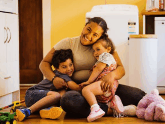 Mother hugs her two young children on the floor of a warm family home in Porirua.