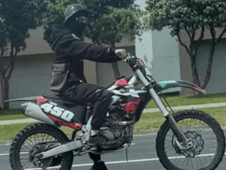 A person wearing a black helmet and face covering rides a black and red dirt bike with the number 450 on the side along a city street in Porirua.