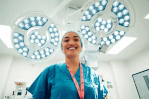 Doctor in surgical scrubs smiles beneath operating theatre lights.