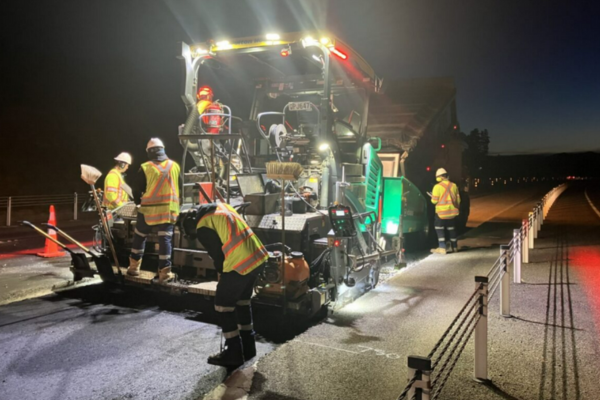 Night-time roadworks underway on Transmission Gully, with workers operating paving machinery under floodlights while traffic lanes are closed.