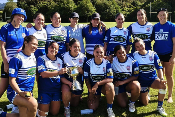 Norths Women's rugby team posing with the Eleanor Roosevelt Cup on a rugby field after their tournament win.