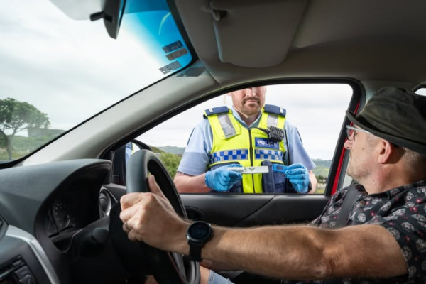 Police officer conducting a roadside saliva drug test during a traffic stop in Porirua.