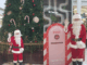 Santa Claus stands beside a North Pole-themed post box display at North City Shopping Centre, waving in front of a large decorated Christmas tree.