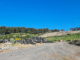 Gravel access road leading through a partially filled landfill site with earth embankments and vegetation under a clear blue sky.