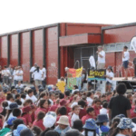 A large group of children and young people sit outdoors facing a stage during a community event hosted by Wesley Community Action.