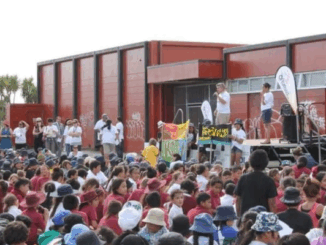 A large group of children and young people sit outdoors facing a stage during a community event hosted by Wesley Community Action.