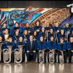 Members of Porirua City Brass pose for a formal group photo, wearing blue jackets and holding brass instruments.