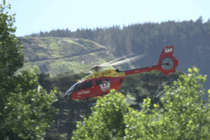 A Westpac Life Flight search and rescue helicopter flies above bush-covered hills near Paekākāriki Hill.