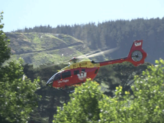A Westpac Life Flight search and rescue helicopter flies above bush-covered hills near Paekākāriki Hill.