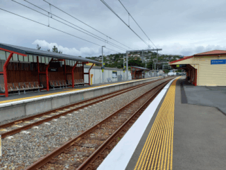 Plimmerton railway station platforms with empty tracks, shelters and overhead power lines on a cloudy day.