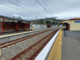 Plimmerton railway station platforms with empty tracks, shelters and overhead power lines on a cloudy day.