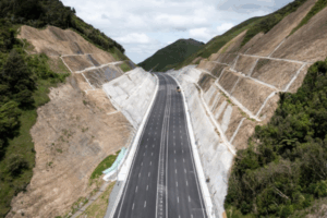 A newly built multi-lane motorway runs through a steep valley with reinforced rock faces on both sides.