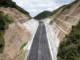 A newly built multi-lane motorway runs through a steep valley with reinforced rock faces on both sides.