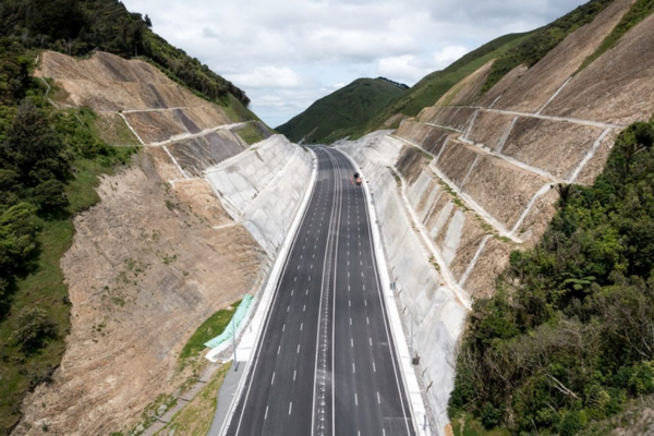 A newly built multi-lane motorway runs through a steep valley with reinforced rock faces on both sides.