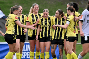 Wellington Phoenix players in yellow-and-black kits celebrate together after scoring during an A-League Women match.