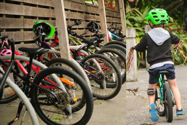 A row of children’s bicycles parked under a wooden shelter at school, alongside a young child wearing a bright green helmet riding a small bike along a footpath.