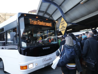 A bus displaying “Train Replacement” picks up commuters at a crowded Wellington station platform.