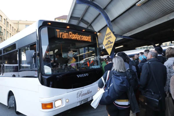 A bus displaying “Train Replacement” picks up commuters at a crowded Wellington station platform.