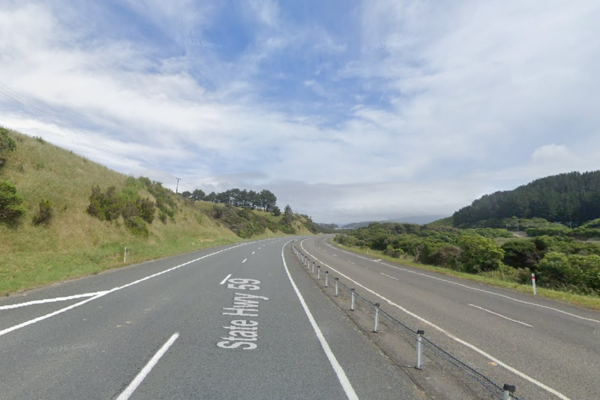 A divided section of State Highway 58 in Porirua, with two lanes in each direction separated by flexible median posts, curving through green hills under a partly cloudy sky.