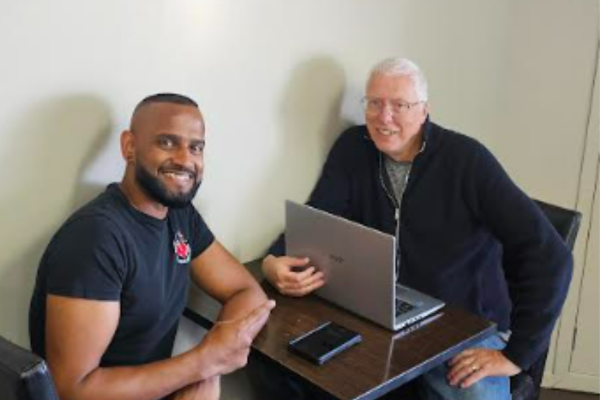 Rodney Strong and café owner Sushil sit at a table at Musclechef café in Aotea where Strong often writes his books.