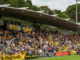 Crowd of Wellington Phoenix supporters in yellow and black fill a covered stand at Porirua Park during a match.