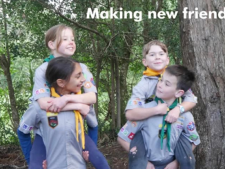 Four children in scout uniforms playing in a wooded area, with two giving piggyback rides, smiling and interacting. Text reads “Making new friends”.