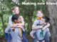 Four children in scout uniforms playing in a wooded area, with two giving piggyback rides, smiling and interacting. Text reads “Making new friends”.