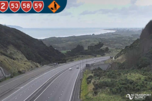 Wide view of a multi-lane highway near Porirua coastline, with light traffic travelling between hills and the sea under cloudy skies.