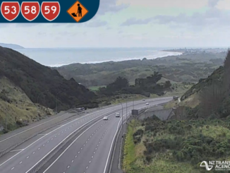 Wide view of a multi-lane highway near Porirua coastline, with light traffic travelling between hills and the sea under cloudy skies.