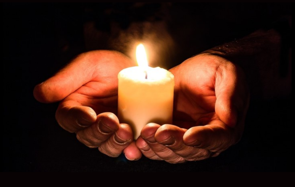 Hands hold a lit candle in the dark.