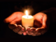 Hands hold a lit candle in the dark.