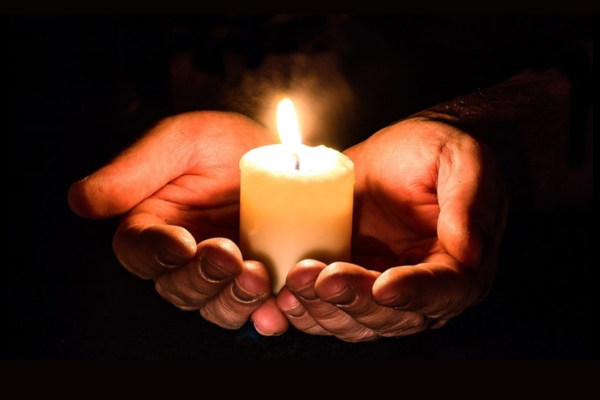 Hands hold a lit candle in the dark.