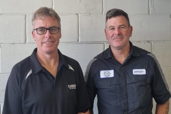 Mike and Anthony Butler standing in workshop uniforms at City Centre Motors in Porirua ahead of the business’s 50th anniversary.