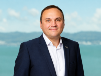 Former Porirua mayor Nick Leggett wearing a navy suit and white shirt, standing in front of a blurred waterfront backdrop.