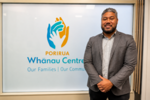 Nu'ulelei Taulalo stands beside Porirua Whānau Centre signage.