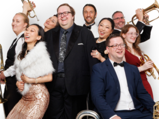 Porirua City Brass performers pose in formal and cabaret-style clothing, smiling and holding brass instruments.