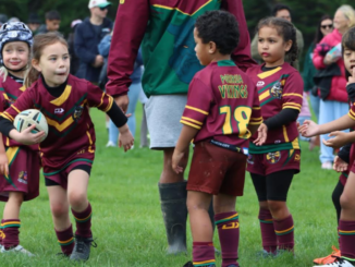 Young Porirua Vikings junior rugby league players in maroon and green uniforms take part in a game on a grass field, with one child running forward carrying the ball.